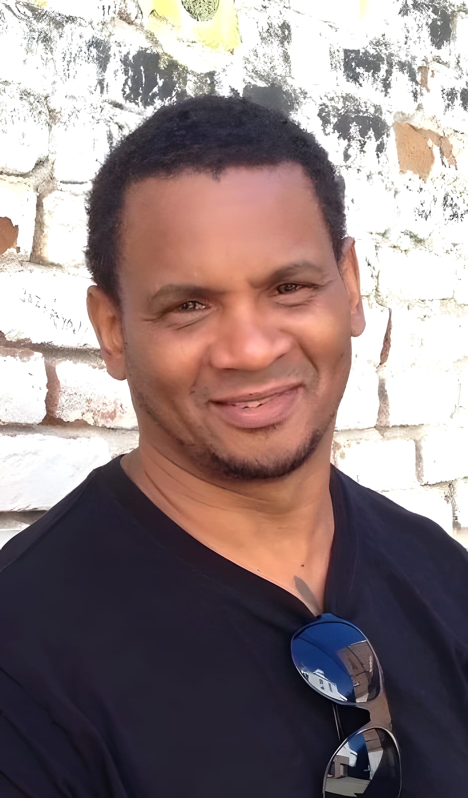 Smiling team member in a black shirt against a brick wall