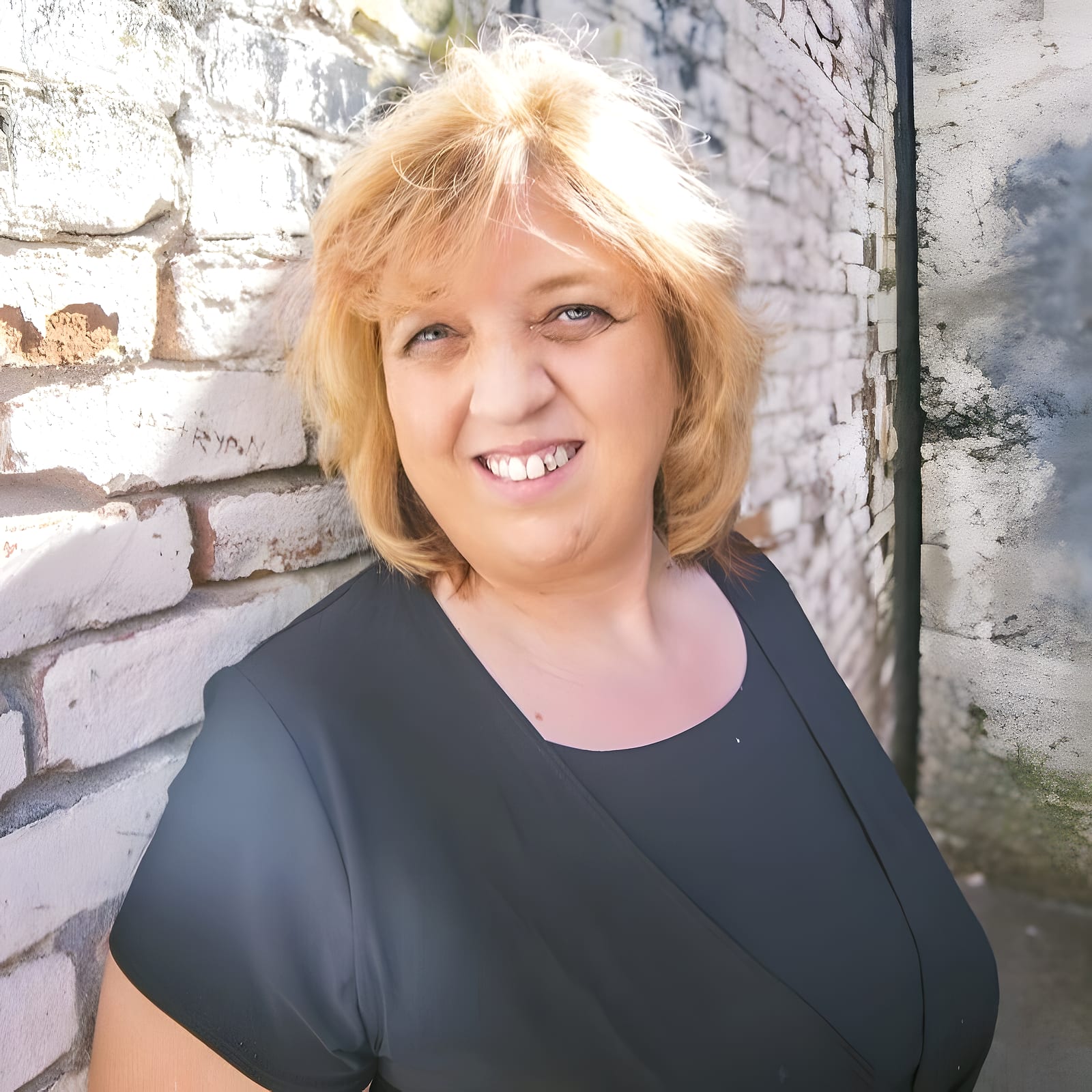 Smiling blonde team member in a black top against a brick wall