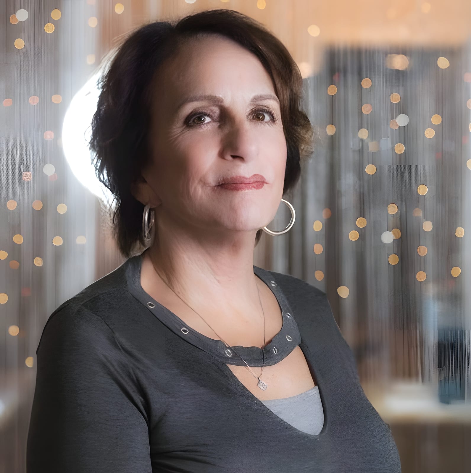 Team member with short dark hair and hoop earrings, salon lights behind her