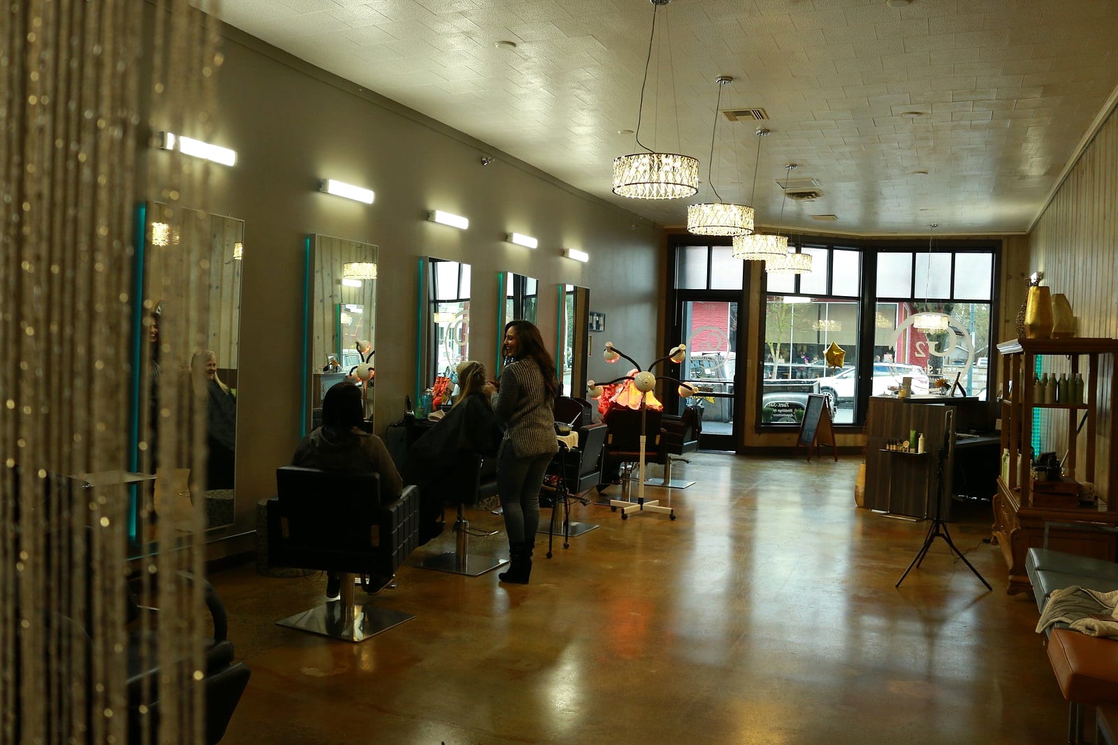 Stylists at work among a row of styling chairs and mirrors, storefront windows behind